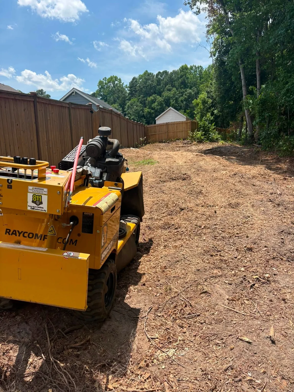 After: cleared area beside a fence with stump grinding equipment