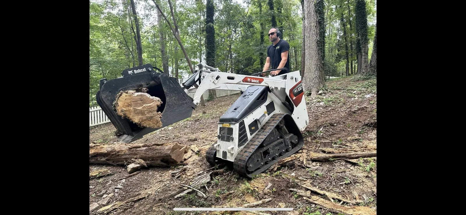 Compact loader moving a cut tree section