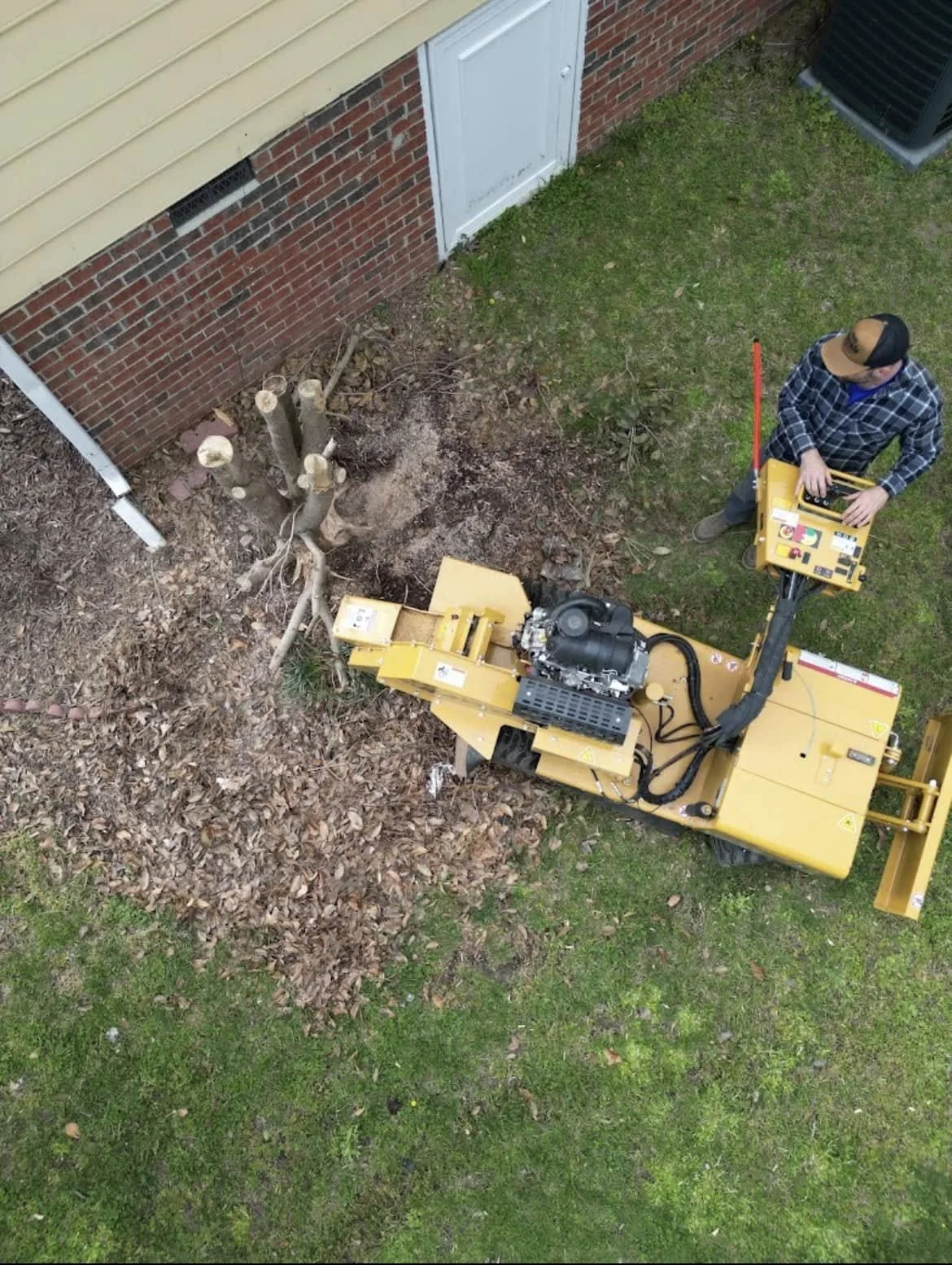 Overhead view of stump grinding beside a house